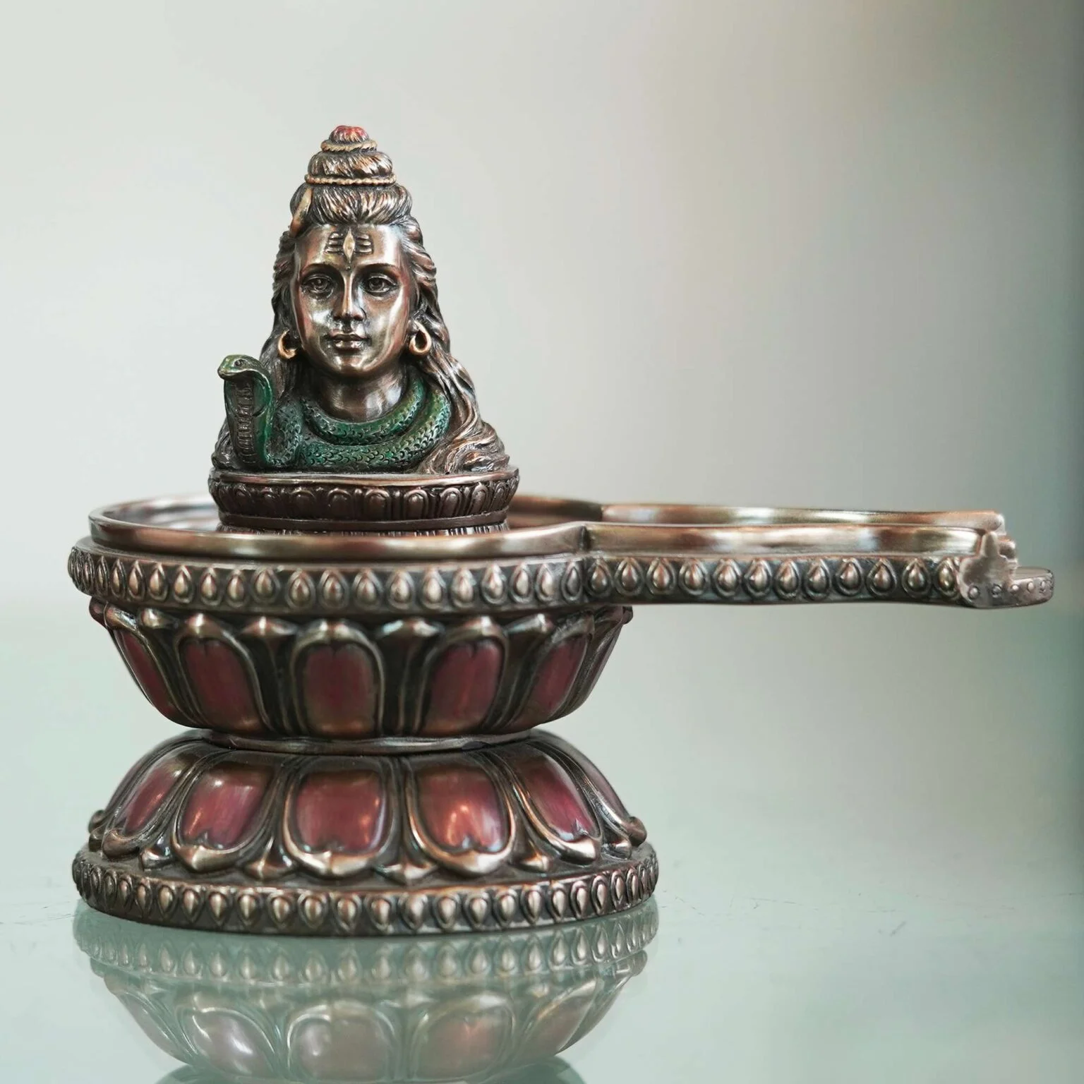 Decor Home Craft A detailed **Shiva Ling Bronze idol to decorate Home Hotel Office Garden 13x13cm BZ-SL1** featuring a sculpted face, resembling a deity, with intricate patterns and a handle, set against a soft grey background, perfect for enhancing the ambiance of a hotel lobby.