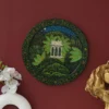 Decor Home Craft Handmade Pichwai Painting depicting a classical temple in a lush forest setting, hung on a deep red wall in a hotel, accompanied by a white orchid and golden sculpture to the side.