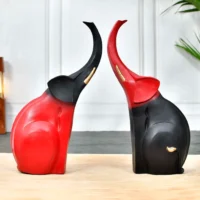 Decor Home Craft Two decorative Polyresin Elephant to Decor Home Showpiece Figurines, one red and one black, facing each other with their trunks raised, set on a wooden surface against a soft-focus background.